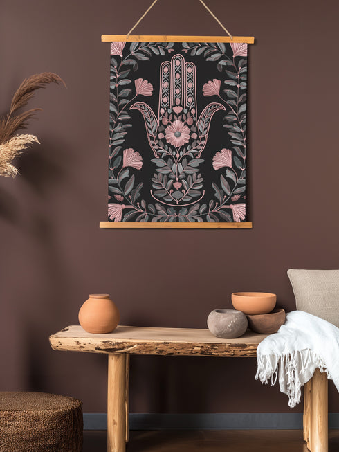 Botanical Hamsa wall tapestry featuring intricate rose gold and teal design on black background, showing a protective hand symbol surrounded by leaf motifs and floral elements, hanging from wooden dowels with natural twine.